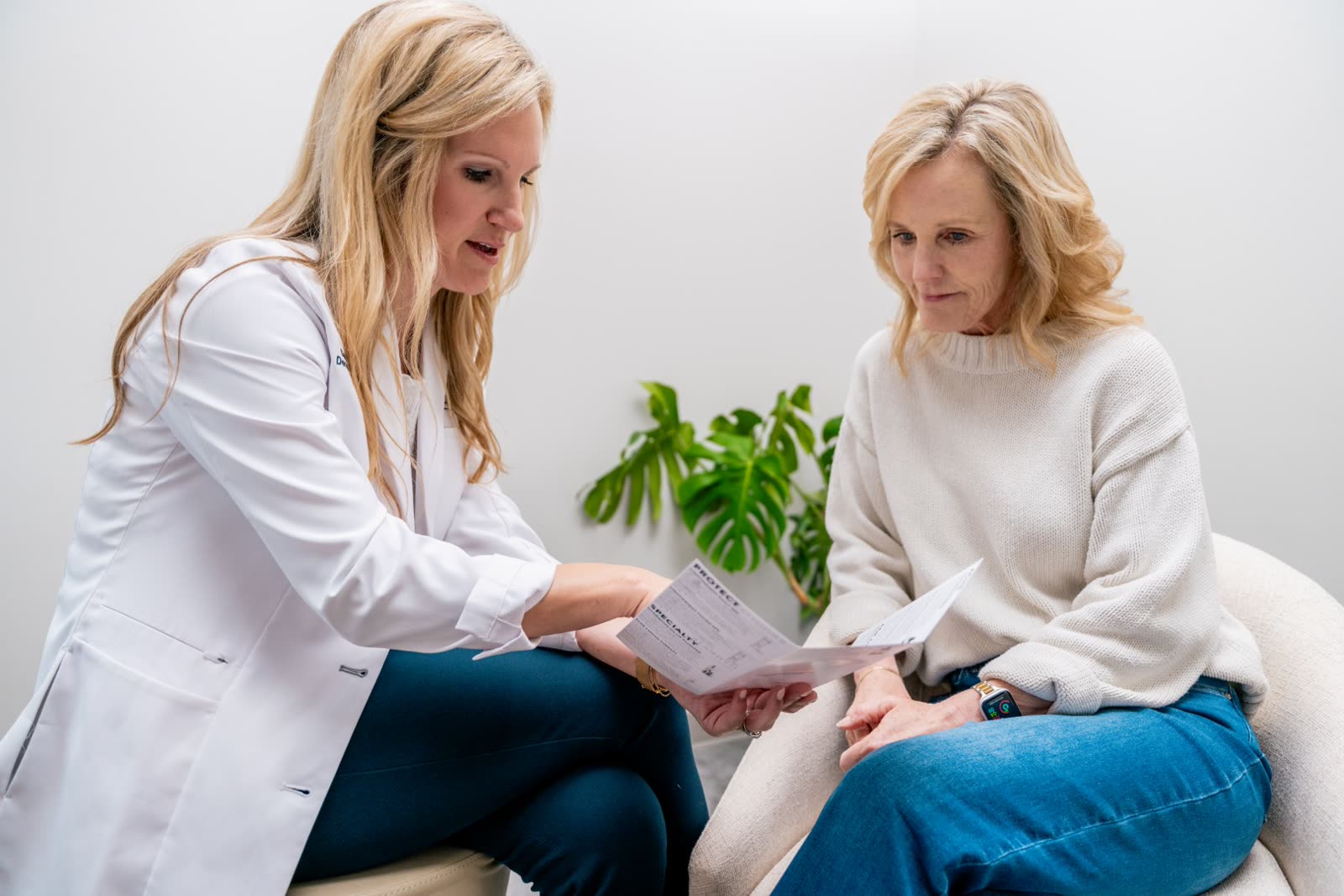 Sarah Wilson, MD, in a white coat, going over a printed treatment plan with a seated guest